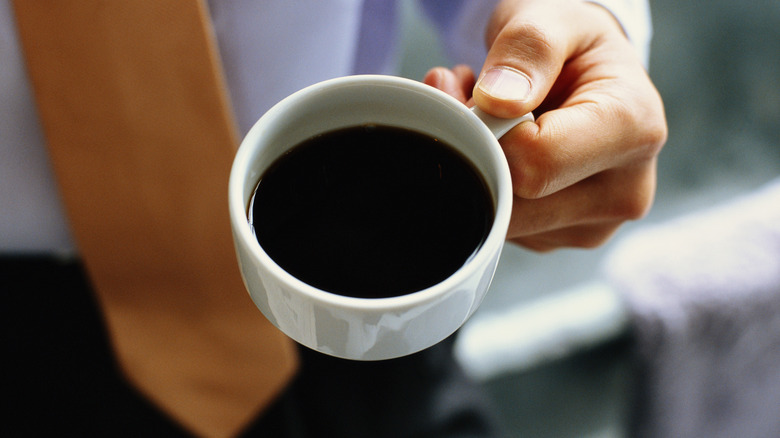 Hand holding white mug of coffee