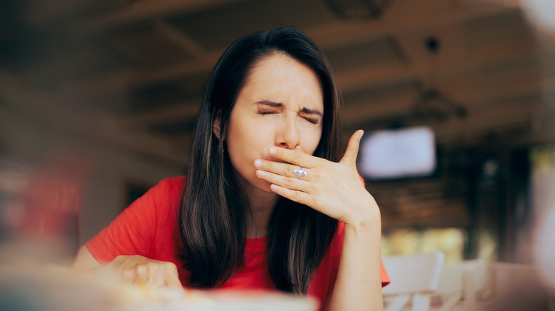 person covering their mouth looking pained while eating