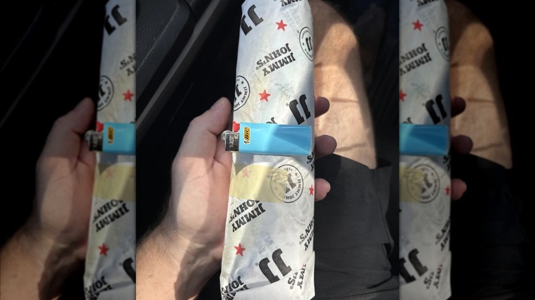 Hand holding wrapped Jimmy John's sandwich with Bic lighter on top, mirrored image