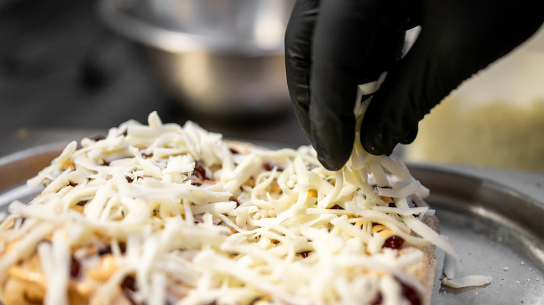 Gloved hand sprinkling cheese on pizza