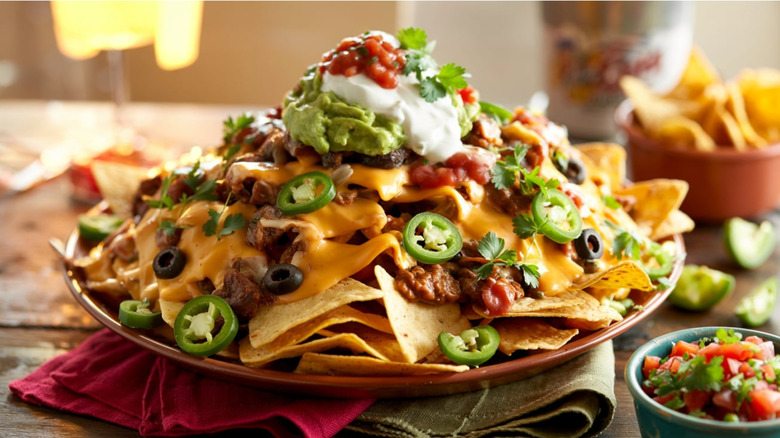 Loaded nachos piled high with toppings on orange plate