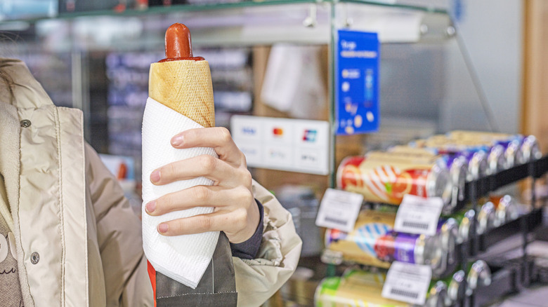 Person holding a hot dog in a gas station