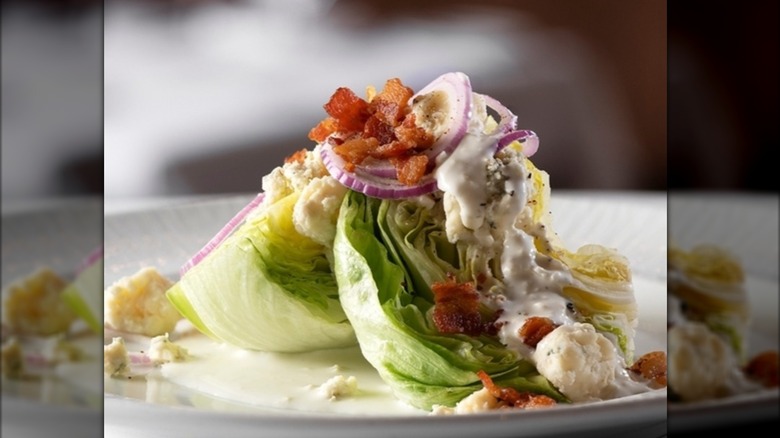 close up of a wedge salad on white plate on light brown table cloth