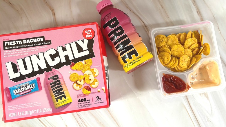 Lunchly nachos box next to strawberry banana Prime and nachos on marble surface