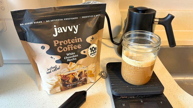 Bag of Javvy protein coffee on kitchen counter next to frother, gooseneck kettle, jar of coffee on scale
