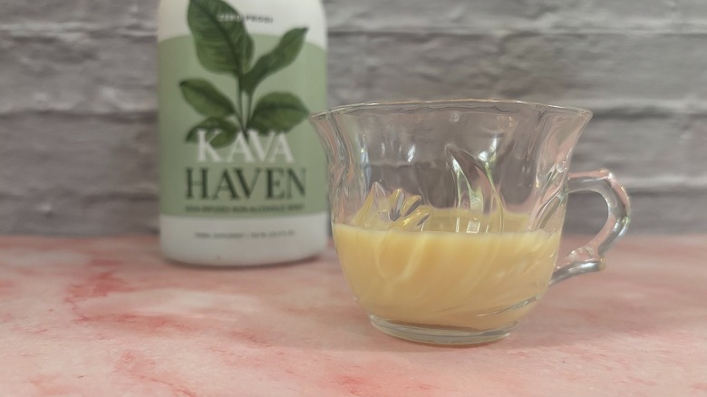 Glass teacup of kava beverage in front of Kava Haven bottle on pink surface