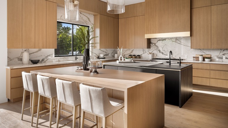 Large kitchen with white stools at wooden island, wooden cabinetry, marble backsplash