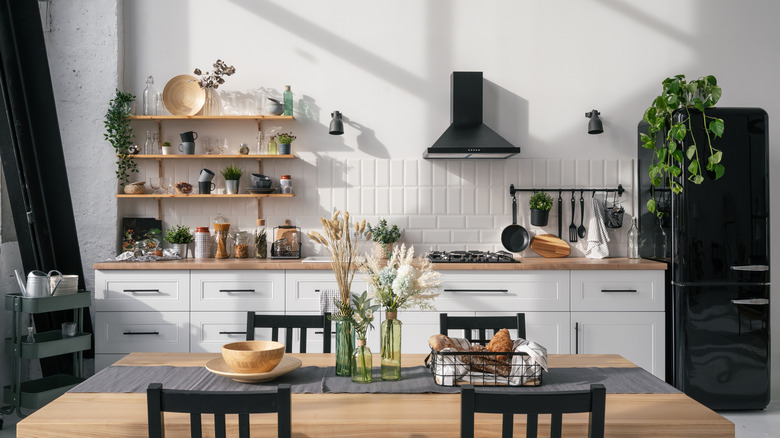 White and wooden kitchen with open shelving, wooden dining table, plant accents, black fridge