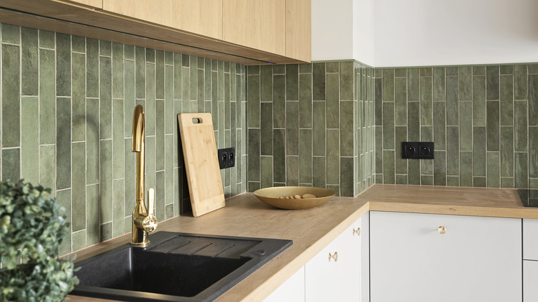 Tiled kitchen backsplash in various shades of sage green, wooden counter