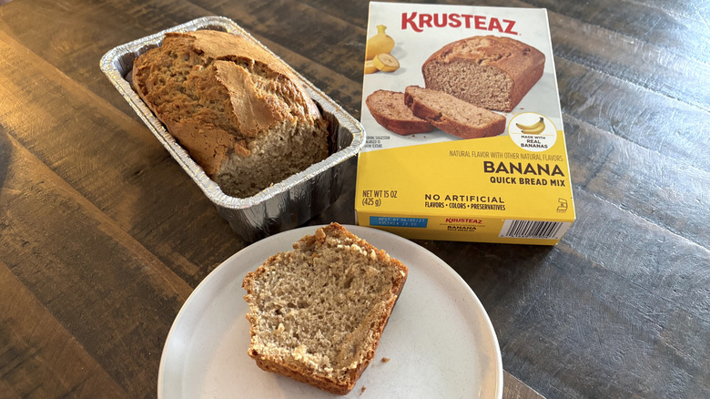 Krusteaz banana quick bread mix in a box next to a loaf in a tin and slice on a plate.