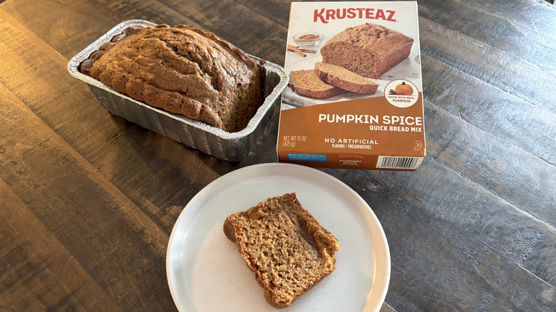 Krusteaz pumpkin spice quick bread mix in box next to a loaf in a tin and a slice on plate.