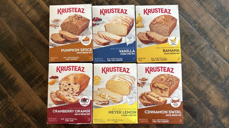Six boxes of Krusteaz pound cake and quick bread mixes on wooden table.