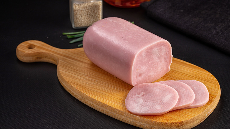Loaf of pork deli meat with slices on wooden board