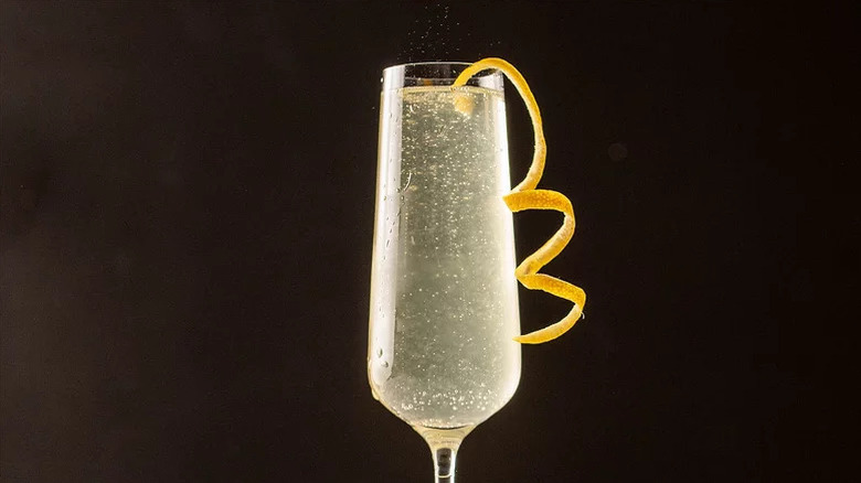 French 75 in champagne flute with lemon garnish against black background