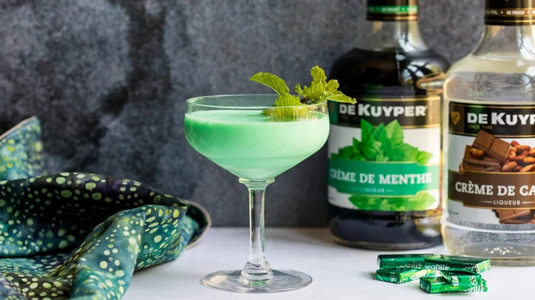 Grasshopper cocktail in coupe glass and mint garnish with DeKuyper bottles in background