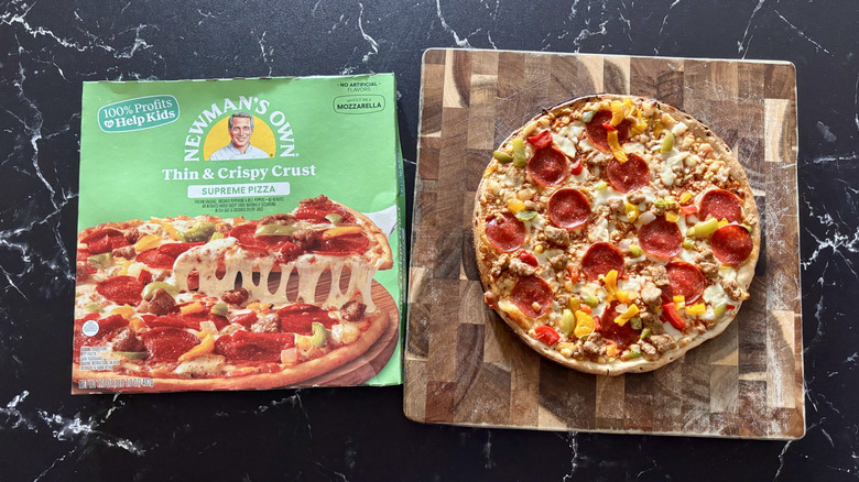 Newman's Own supreme pizza box next to supreme pizza on wooden board