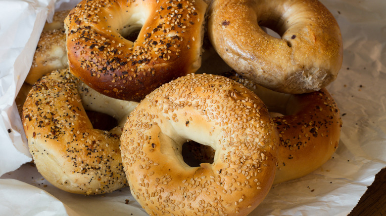 Sesame, cinnamon raisin, and everything bagels spilling out of a white paper wrapping.