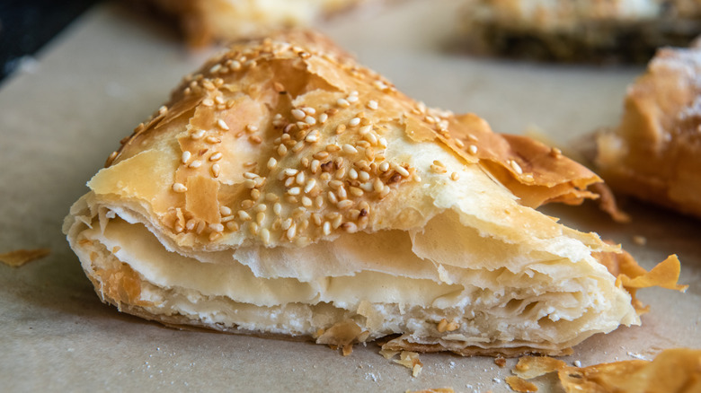Tiropita, a layered Greek pastry made with phyllo dough and topped with sesame seeds, on a tray with parchment paper.