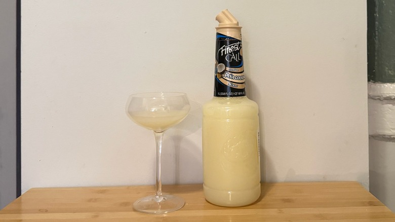 bottle of Finest Call piña colada mix with a glass filled next to it