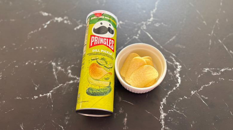 Tube of dill pickle Pringles next to Pringles in bowl