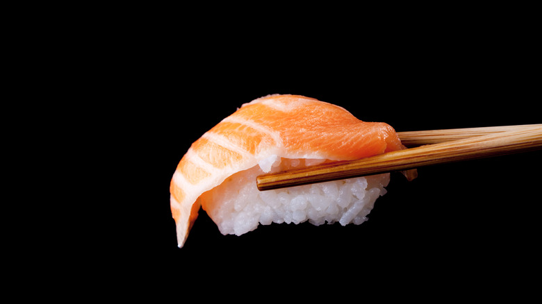 Sushi featuring salmon on white rice being held by chopsticks