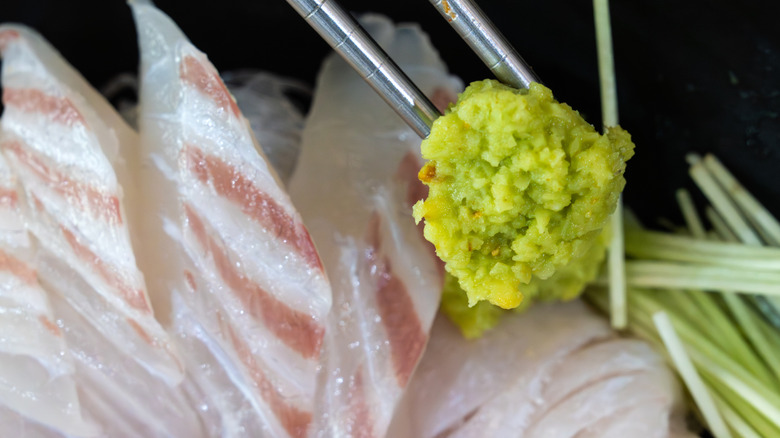 A lump of green wasabi on white fish held by chopsticks