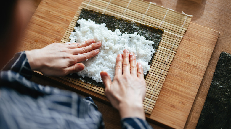 Hands pressing sushi rice into a piece of seaweed
