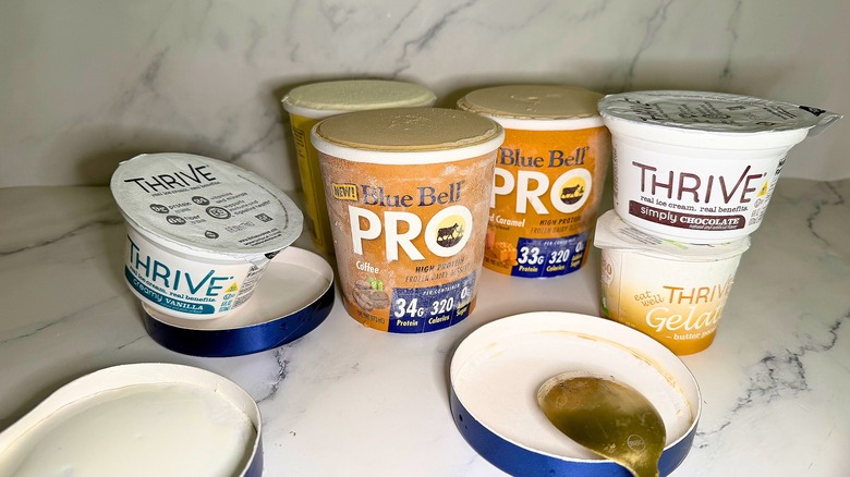 Several containers of Blue Bell protein ice cream and Thrive gelato on marble surface