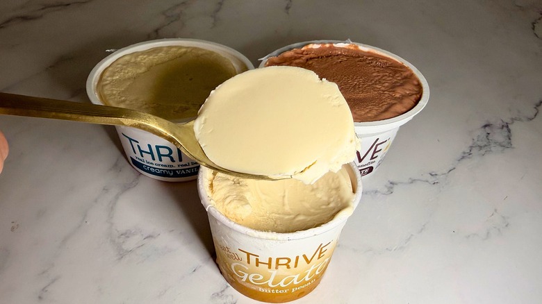 Hand holding spoonful of Thrive ice cream over three pints of ice cream on marble surface
