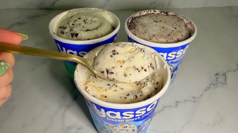 Hand holding spoonful of Yasso ice cream over three pints of ice cream on marble surface