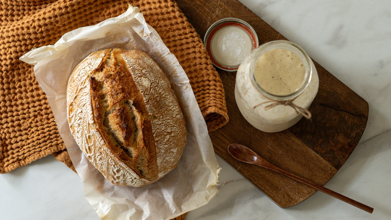 A loaf of sourdough bread next to a jar of starter