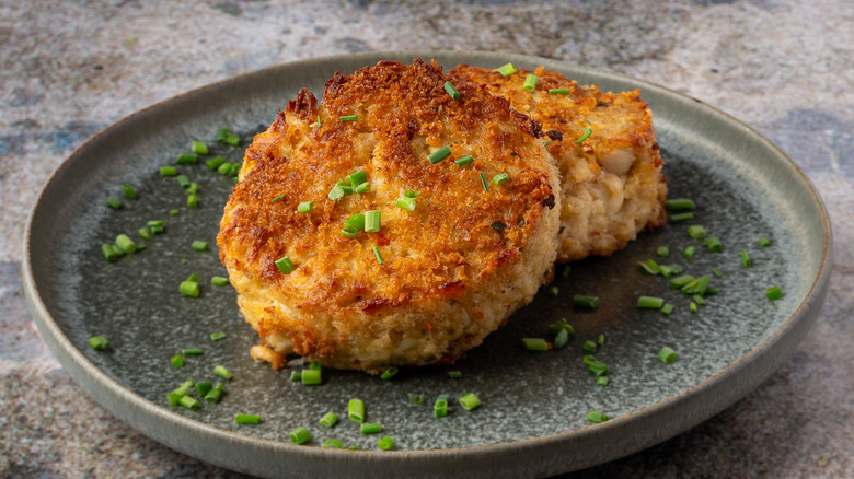 Two crab cakes on a plate with chives.