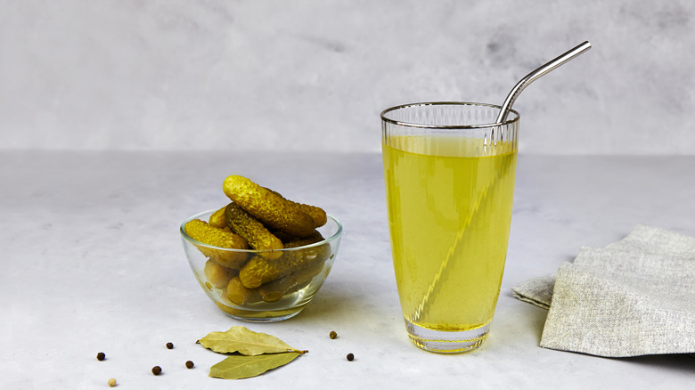 Pickle brine in a glass next to a ramekin of pickles