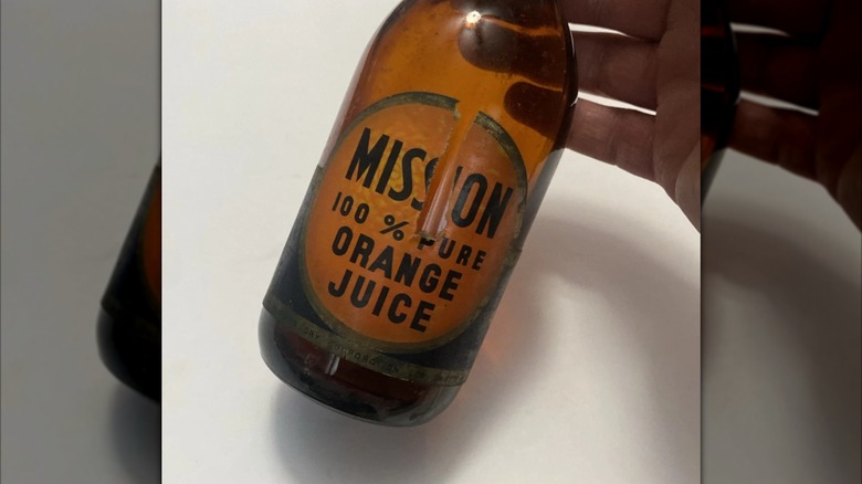 Mirrored image of hand holding vintage glass bottle of Mission orange