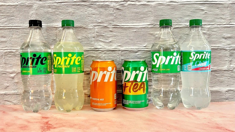 Six sprite bottles/cans lined up on pink table