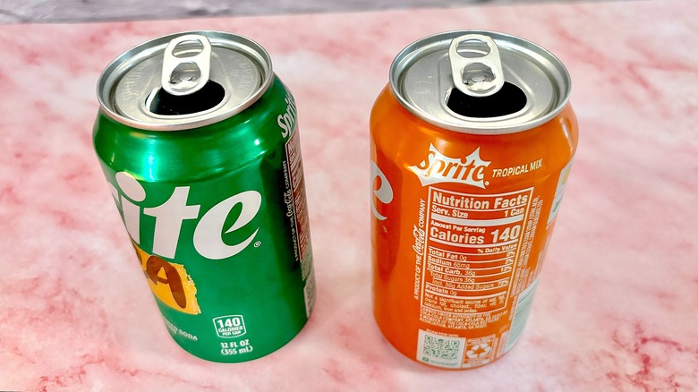 Two open cans of Sprite on pink marble surface