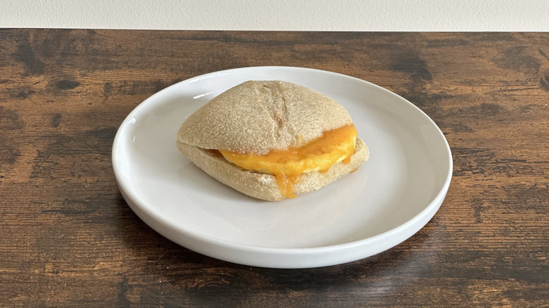Wooden table with white plate featuring an egg and cheese sandwich on a bun