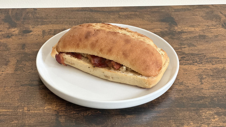 Wooden table with white plate with chicken bacon sandwich
