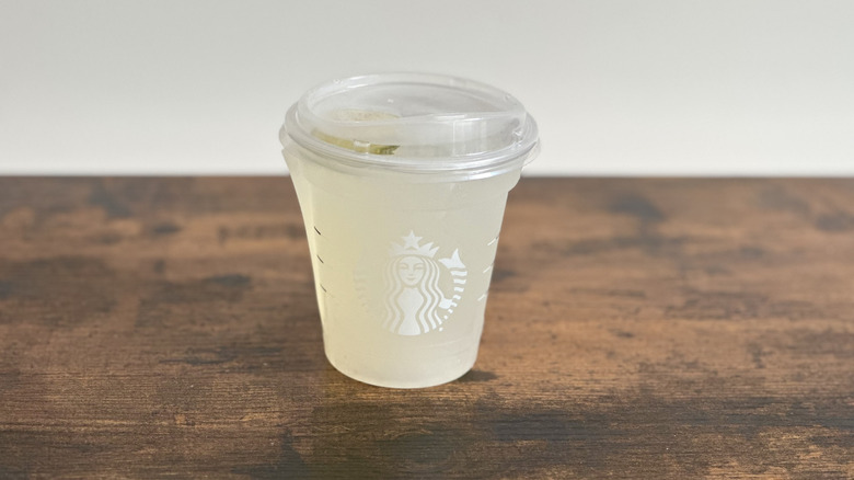 Wooden table with plastic cup of Starbucks Cool Lime Lemonade Refresher