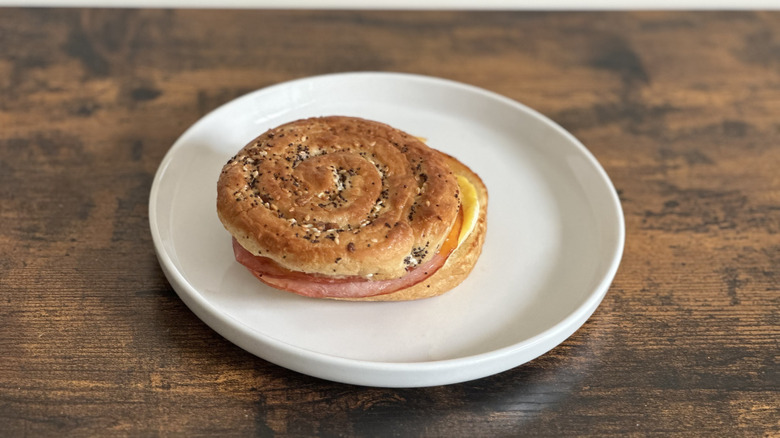 Wooden table with white plate with sandwich of everything croissant bun, ham, egg, and cheese