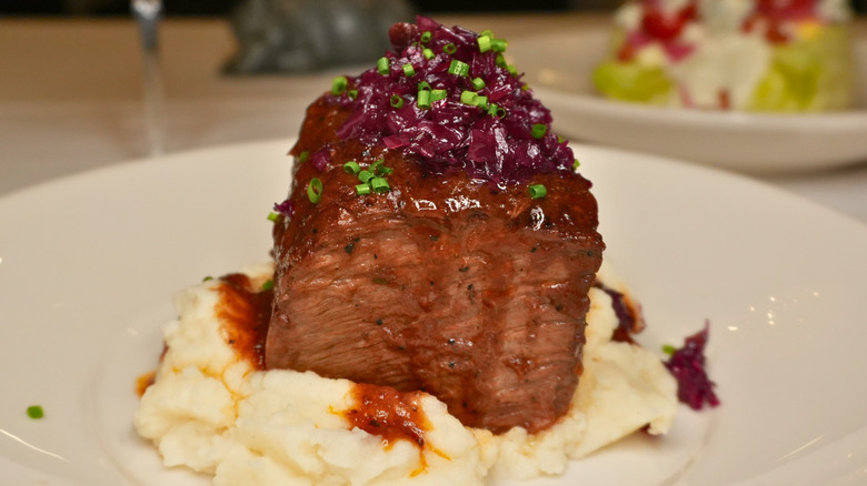 A hunk of Morton's wagyu ribeye sitting in a pool of its own fat on a white plate. The steak is topped with a generous dab of seasoned butter.