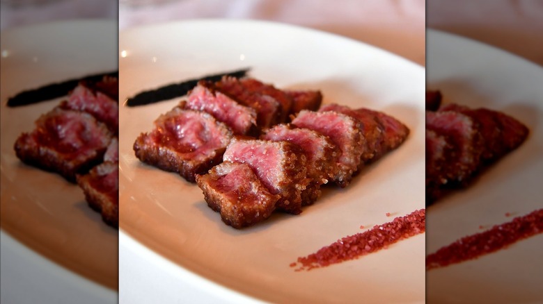 Two rows of medium-rare, sliced A5 Japanese wagyu beef on an oblong white plate, with red and black seasonings along the sides.