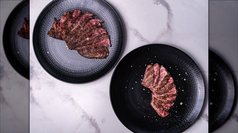 Two Wagyu steaks on blue and black plates sit on a marble countertop.