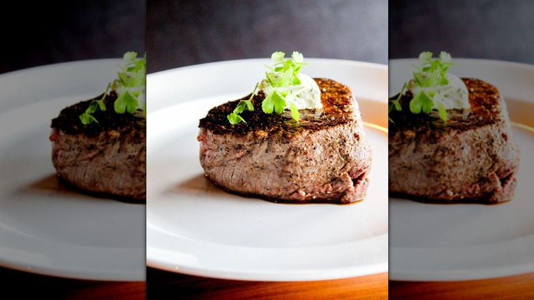 Filet mignon on a white plate, topped with greenery