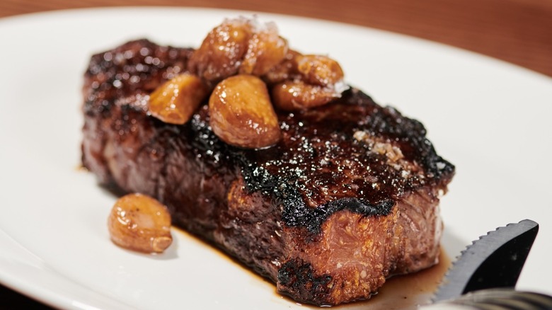 NY strip on a white plate topped with pickled garlic