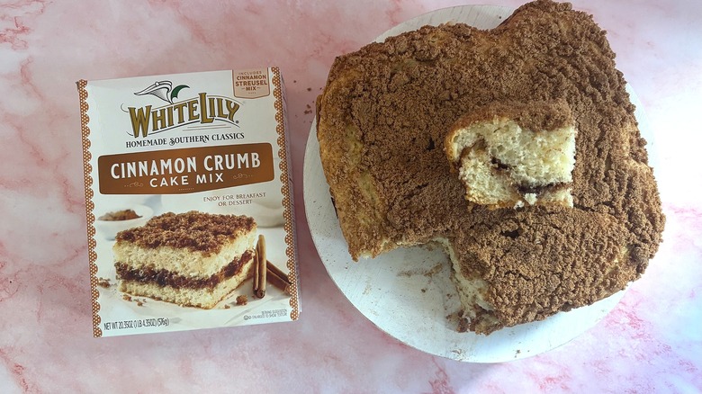 Overhead shot of box of White Lily coffee cake mix next to coffee cake with slice removed on white platform