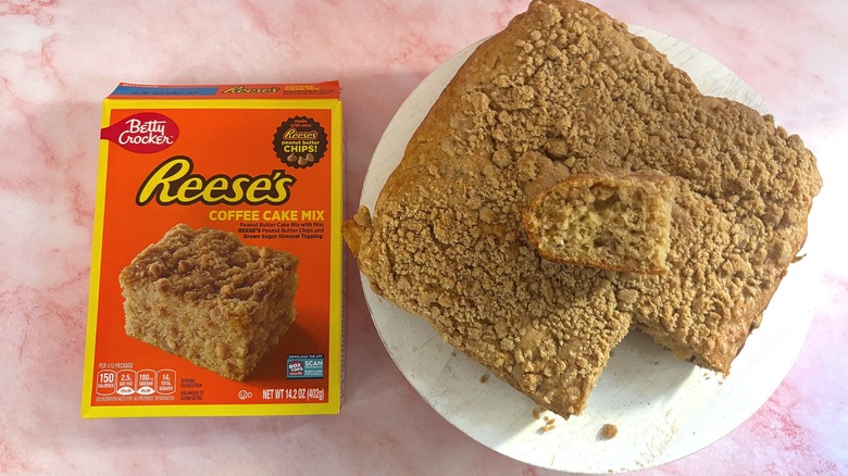 Overhead shot of box of Reese's coffee cake mix next to coffee cake with slice removed on white platform