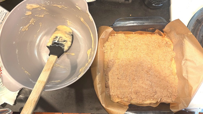 Top-down shot of dirty mixing bowl next to coffee cake batter in pan, all on black counter