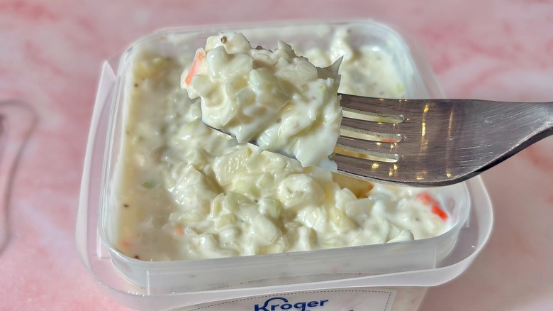 Forkful of coleslaw held above coleslaw container on pink surface