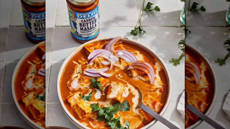 Jar of cashew butter masala simmer sauce beside a fully prepared curry topped with onions